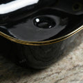 Glossy finish detail on black and gold ceramic bathroom sink, rectangular tabletop vessel basin rim close-up